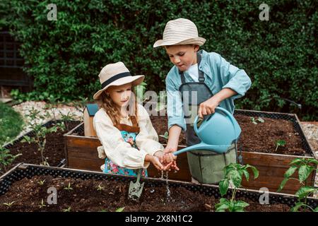 Fille et garçon prenant soin de petites plantes de légumes dans un lit surélevé, tenant une petite pelle. Enfance en plein air dans le jardin. Banque D'Images