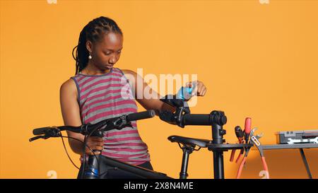 Travailleur joyeux installant le stand de réparation de vélo avant d'entretenir les roues défectueuses, fond de studio. Réparateur heureux fixant le vélo sur le support de travail avant de réparer les composants Banque D'Images