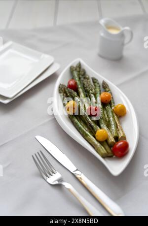 Une source de grandes fibres alimentaires, asperges vertes cuites au four servies dans une assiette blanche, comme plat d'accompagnement avec tomates colorées et sauce hollandaise Banque D'Images