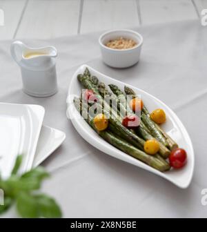 Une source de grandes fibres alimentaires, asperges vertes cuites au four servies dans une assiette blanche, comme plat d'accompagnement avec tomates colorées et sauce hollandaise Banque D'Images