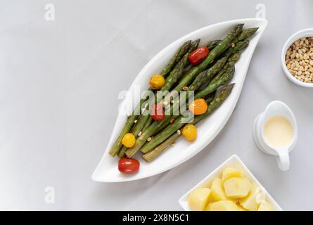 Une source de grandes fibres alimentaires, asperges vertes cuites au four servies dans une assiette blanche, préparées comme plat d'accompagnement avec des tomates colorées Banque D'Images