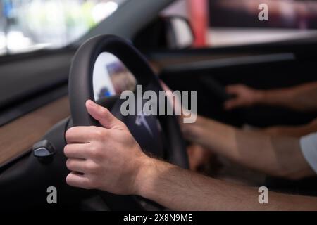 Derrière le volant Tesla modèle y voiture électrique, mains masculines sur la colonne du conducteur, voiture de tourisme moderne, présentant des caractéristiques intérieures telles que la roue de contrôle Banque D'Images