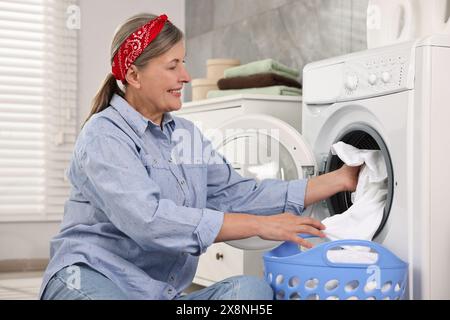 Heureuse femme au foyer mettant le linge dans la machine à laver à la maison Banque D'Images