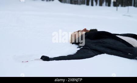 Heureux jeune homme dans la forêt hivernale de conte de fées couché sur la neige. Support. Concept de religion et sentiment d'unité avec la nature. Banque D'Images
