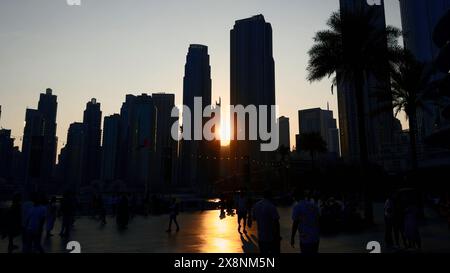 Coucher de soleil entre les tours de gratte-ciel et la marche méconnaissable foule de gens. Action. Quartier central de la ville de Dubaï. Banque D'Images