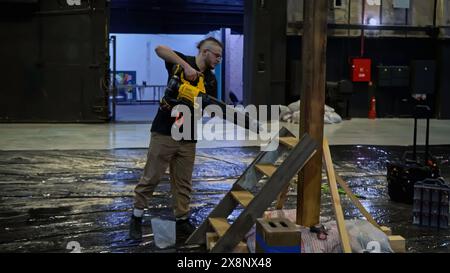 Jeune ouvrier masculin utilisant un ventilateur de construction pour nettoyer les escaliers en bois assemblés et le pilier de la sciure de bois, des copeaux de bois. Support. Préparation de la scène Banque D'Images