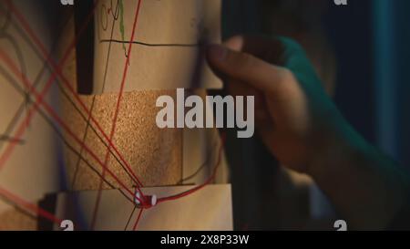 Gros plan du tableau avec des notes et des fils. Film de stock. L'homme enquête et fixe des preuves à bord. L'homme vérifie les photos et les notes sur la recherche Banque D'Images