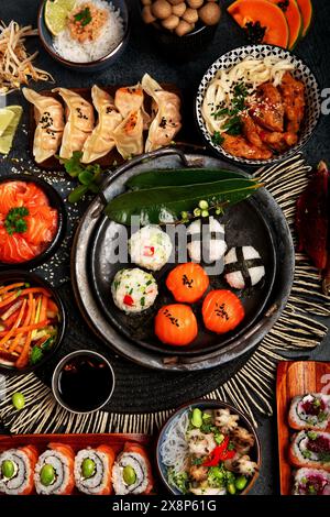 Sushi et cuisine japonaise sur un fond sombre. Rouleaux de sushi, soupe, riz frit, nigiri, sauce soja, baguettes. Cadre alimentaire asiatique/japonais. Vue de dessus. Banque D'Images