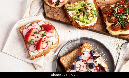Divers sandwichs végétaliens sur un fond clair. Toasts sains avec fromage, avocat, roquette, tomates et houmous. Alimentation saine. Vue de dessus. Banque D'Images