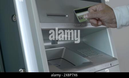 Gros plan d'un homme retirant de l'argent au distributeur automatique. Support. Distributeurs automatiques modernes avec retrait d'argent sans contact. L'homme met la carte au terminal et retire de l'argent Banque D'Images