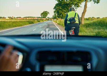 Cycliste fait du vélo sur la route de campagne devant la voiture. Situation dangereuse sur route Banque D'Images