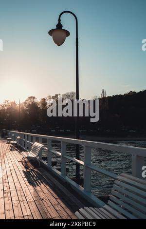 Blanc Vieux ponton de pont en bois contre beau fond naturel de ciel de coucher de soleil, fond d'écran scène de mer polyvalente. Bancs blancs pas de gens à Gdynia Orlowo, Pologne. Jetée en bois, molo avec marina et plage destination touristique Banque D'Images