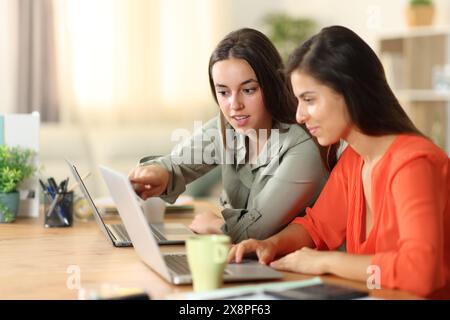 Deux télétravailleurs travaillant ensemble discutent et vérifient leur ordinateur portable à la maison Banque D'Images