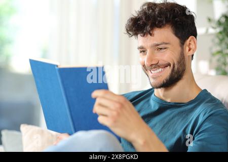 Homme heureux lisant un livre en papier assis sur un canapé à la maison Banque D'Images