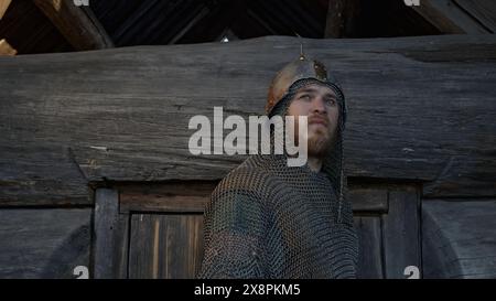 Ancien bogatyr russe debout par poutre en bois mur izba et sifflement. Support. Concept d'anciens héros de contes de fées russes. Banque D'Images