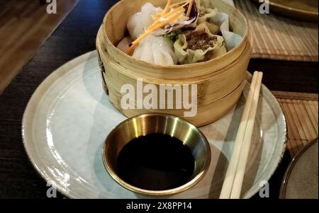 Dim sum serti dans un plateau vapeur en bambou, petite portion de sauce soja et baguettes à côté Banque D'Images