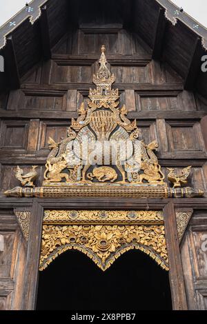 Ancien panneau de bois sculpté doré avec paon au-dessus de l'entrée du monument historique Wat Phan Tao temple bouddhiste, Chiang mai, Thaïlande Banque D'Images