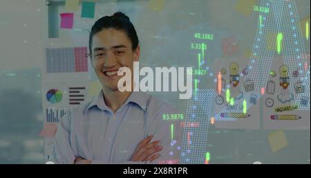 Image de graphiques au-dessus d'un homme asiatique souriant debout les bras croisés contre des rapports et gribouillis sur le mur Banque D'Images