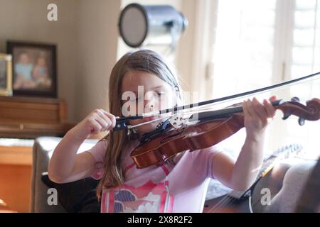 Jeune fille profondément concentrée sur jouer du violon à l'intérieur. Banque D'Images