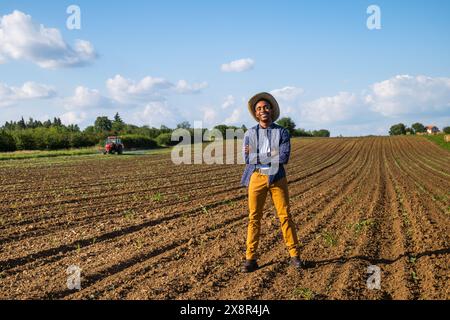 Agriculteur africain se tient debout dans son champ agricole. Il supervise la pulvérisation du champ. Banque D'Images