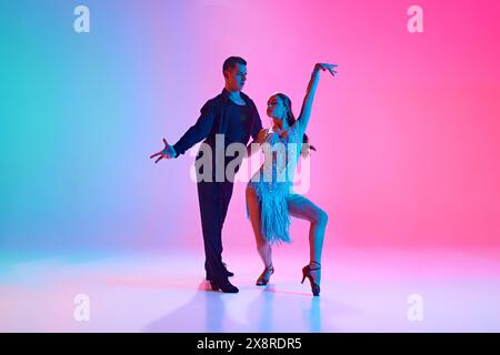 Duo de danseurs de salle de bal, homme et femme, en costumes de scène posant dans un éclairage au néon sur fond dégradé. Banque D'Images