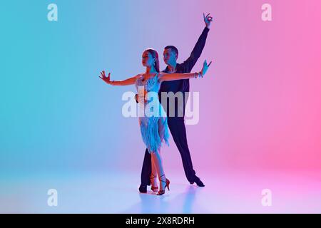 Duo de danseurs de salle de bal, homme et femme en costumes festifs se déplaçant dans un éclairage au néon sur fond dégradé. Banque D'Images