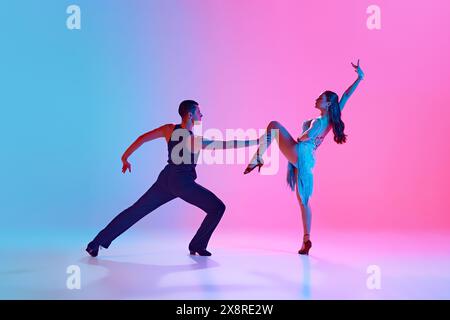 Homme et femme, danseurs de salle de bal, exécutant plein de sentiments danse tango dans un éclairage au néon sur fond dégradé. Banque D'Images