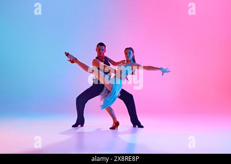 Portrait de jeune couple talentueux pratiquant la danse de salle de bal en mouvement dans un éclairage au néon sur fond dégradé. Banque D'Images