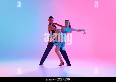 Jeune homme et jeune femme, danseurs de salle de bal dansant expressivement énergique tango dans un éclairage au néon sur fond dégradé. Banque D'Images