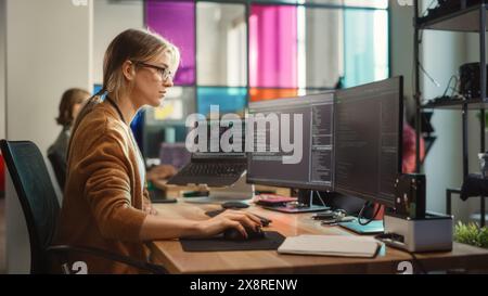 Femme caucasienne codage sur PC de bureau et configuration d'ordinateur portable avec plusieurs écrans dans le bureau spacieux. Ingénieur logiciel junior féminin travaillant sur un nouveau sprint de développement d'applications mobiles pour start-up. Banque D'Images