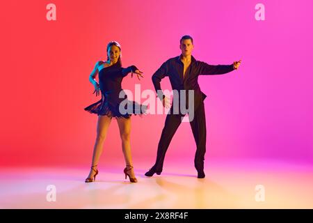 Photo dynamique d'un jeune homme et d'une jeune femme dansant Zumba en mouvement dans un éclairage au néon sur fond dégradé vibrant. Banque D'Images