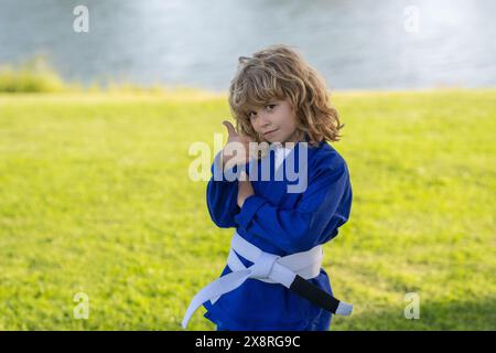 Enfant garçon pratiquant le karaté en plein air. Karaté sport pour enfants. Petit garçon portant un kimono faisant du karaté dans le parc. Boîte de dressage pour enfants. Petit combattant de karaté. Marti Banque D'Images