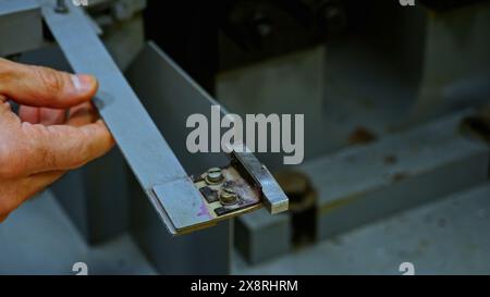 Gros plan des mains de travailleurs mettant de petites tuiles métalliques pour le traitement dans la machine industrielle. Film de stock. Détails de l'atelier. Banque D'Images