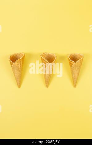 Vue de dessus de trois cônes gaufrés de crème glacée sur fond jaune. Fond d'écran d'été, pose à plat, espace de copie. Banque D'Images