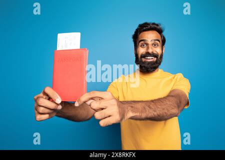 Homme heureux tenant passeport et carte d'embarquement sur fond bleu Banque D'Images