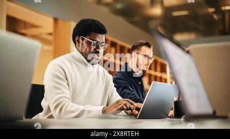 Portrait d'un homme noir enthousiaste tournant sur son ordinateur portable et commençant sa journée de travail au bureau. Graphiste masculin souriant tout en développant un nouveau concept visuel Banque D'Images