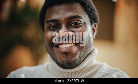Gros plan Portrait d'un jeune homme noir heureux avec barbe taillée, portant un élégant col roulé blanc posant pour l'appareil photo. Directeur afro-américain souriant tout en regardant Camera. Banque D'Images
