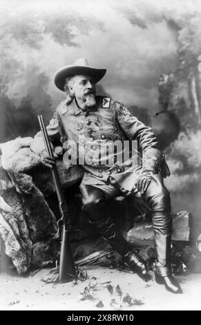 Buffalo Bill Cody, portrait en pied, assis sur des rochers, face à droite, tenant un fusil Banque D'Images