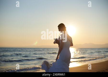 Mariée japonaise marchant sur la plage au coucher du soleil Banque D'Images