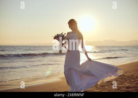 Mariée japonaise marchant sur la plage au coucher du soleil Banque D'Images