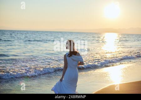 Mariée japonaise marchant sur la plage au coucher du soleil Banque D'Images