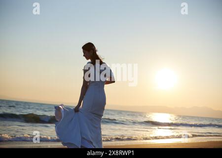 Mariée japonaise marchant sur la plage au coucher du soleil Banque D'Images