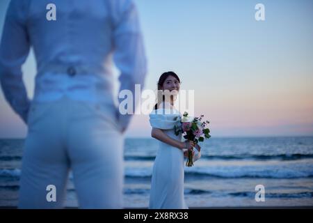 Mariée et mariée japonaises debout sur la plage au coucher du soleil Banque D'Images