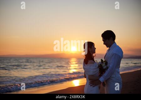 Mariée et mariée japonaises debout sur la plage au coucher du soleil Banque D'Images