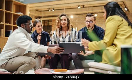 Groupe multiethnique de personnes créatives travaillant sur projet dans un bureau lumineux moderne. Un groupe diversifié de collègues développant une nouvelle approche à l'aide de graphiques, d'ordinateurs portables et de tablettes. Grand angle Banque D'Images