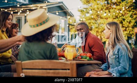 Famille et amis multiethniques divers se réunissant à une table de jardin. Les gens mangeant des légumes grillés et frais, partageant de savoureuses salades pour une grande fête de famille avec des parents. Banque D'Images