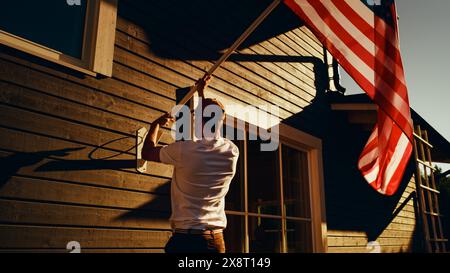 Propriétaire patriotique élevant le drapeau national des États-Unis d'Amérique sur sa maison de quartier. Homme adulte fièrement volant le drapeau sur sa maison de banlieue. Indépendance, liberté, liberté aux États-Unis concept. Banque D'Images