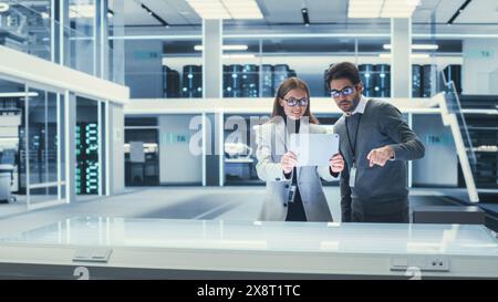 Deux ingénieurs industriels se sont réunis à une table. Jeunes scientifiques féminins et masculins multiethniques utilisant Tablet Computer avec logiciel de réalité augmentée. Banque D'Images