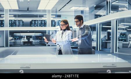 Deux ingénieurs industriels se sont réunis à une table. Jeunes scientifiques féminins et masculins multiethniques utilisant Tablet Computer avec logiciel de réalité augmentée. Banque D'Images