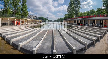 Paris, France - 05 25 2024 : canal de l'Ourcq. Réflexions sur le canal Ourcq des bâtiments résidentiels, pont, barges et arbres de Stalingrad Battle Squa Banque D'Images